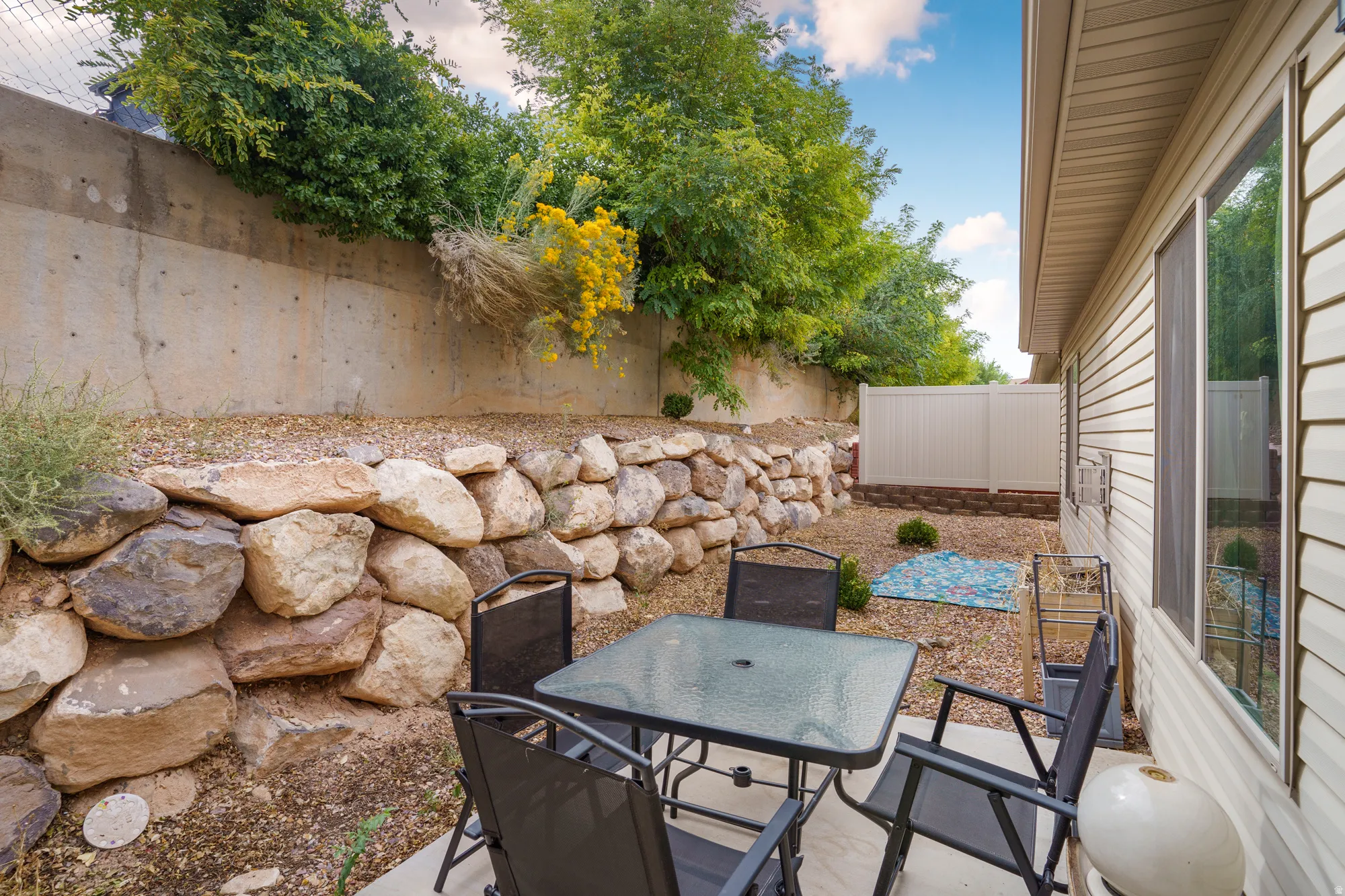 Paved patio area, stone retaining wall, concrete retaining wall, vinyl siding, and a white privacy fence