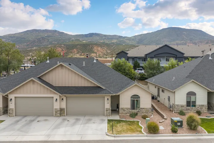 Mountain backdrop, two-car garage, stone facade accents, light-colored siding, and dark-shingle roofing