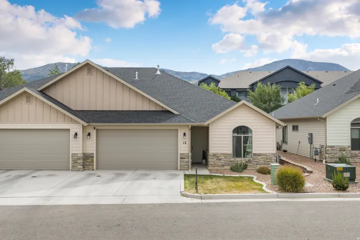 Siding exterior with stone accents, arched window, attached garages, and a paved driveway
