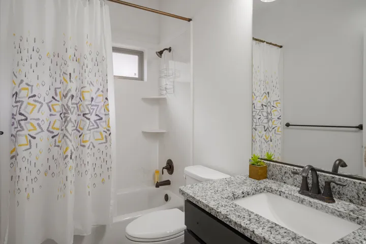 Bathroom featuring a white bathtub, built-in shelving, a shower head with a handheld sprayer, a dark vanity, and a light-colored speckled countertop