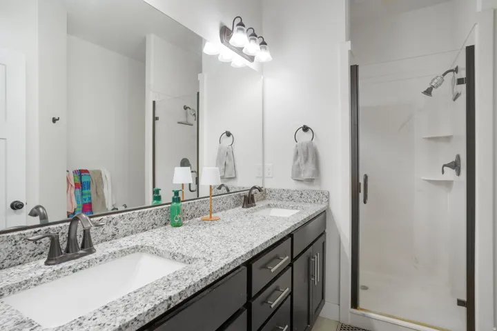 Dual vanity with undermount sinks, speckled countertop, dark wood-finish cabinetry, and a walk-in shower with dark-framed glass enclosure