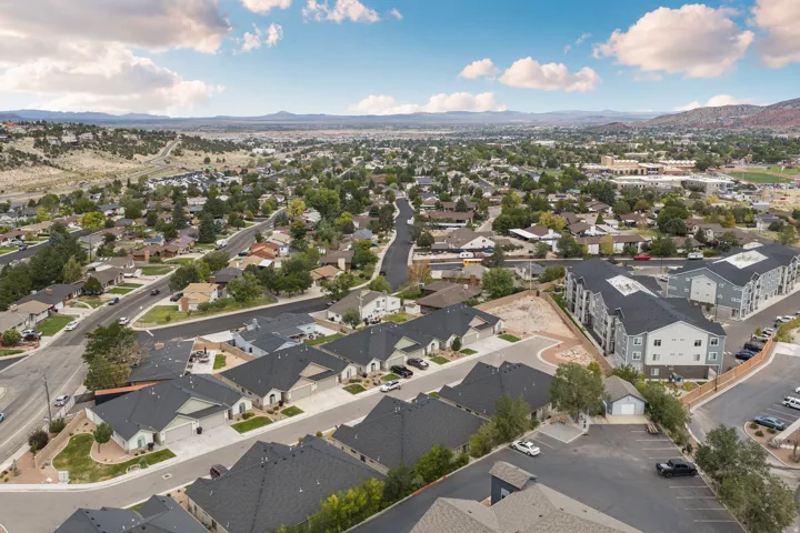 Expansive aerial perspective showcasing a residential neighborhood with varied architectural styles, mature trees, paved streets, and distant mountainous terrain