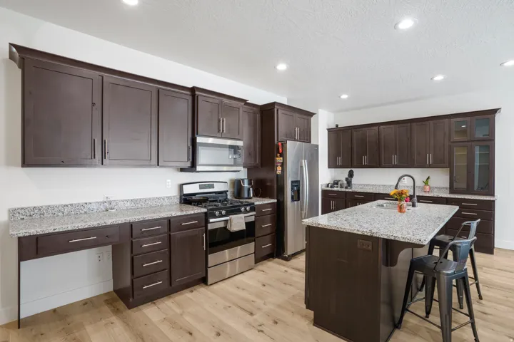 Kitchen featuring wood-finish flooring, dark wood cabinetry, light-toned countertops, a central island with an integrated sink, and stainless steel appliances