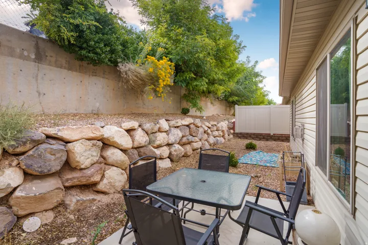 Paved patio area, stone retaining wall, concrete retaining wall, vinyl siding, and a white privacy fence
