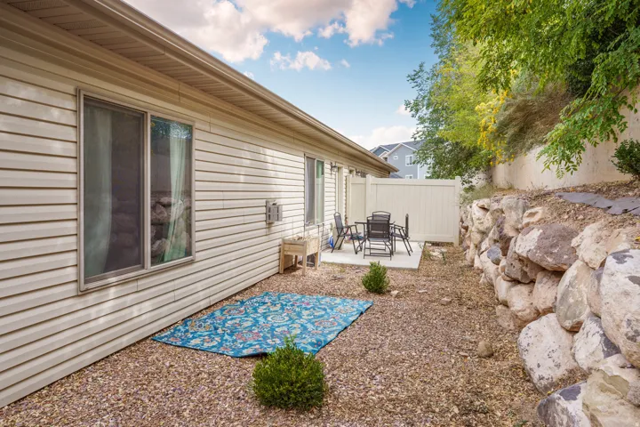 Siding exterior with a built-in patio, concrete slab, and a rock retaining wall