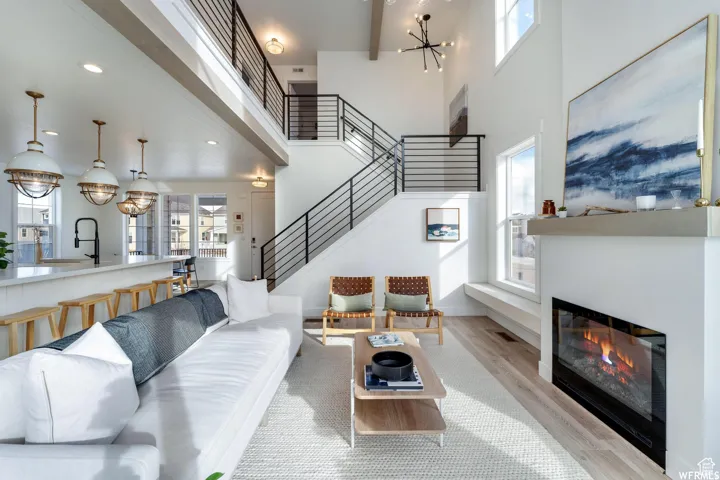 Two-story living area with an open-concept design, wood-finish flooring, a contemporary fireplace, and an exposed beam ceiling