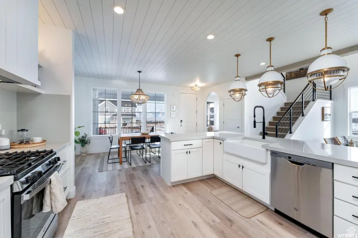 White cabinetry with black hardware, wood-finish flooring, recessed lighting, a farmhouse sink with a gooseneck faucet, and stainless steel appliances