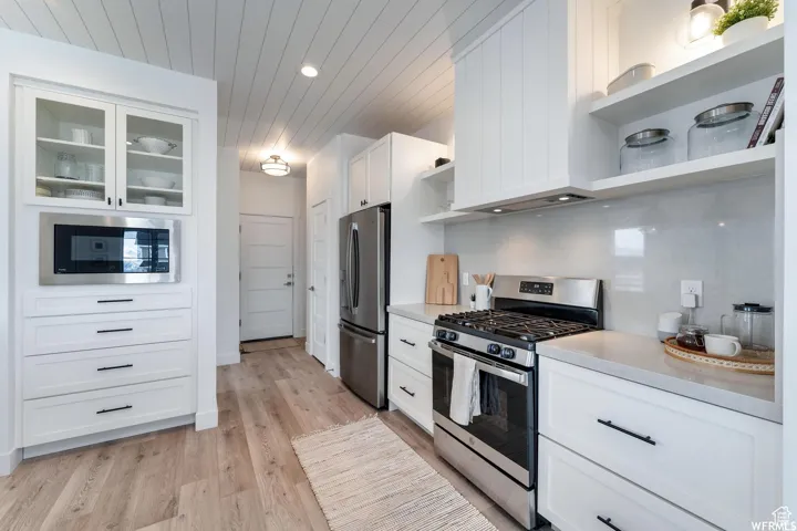 White cabinetry with matte black hardware, stainless steel appliances, wood-finish flooring, white shiplap ceiling, and light-toned countertops