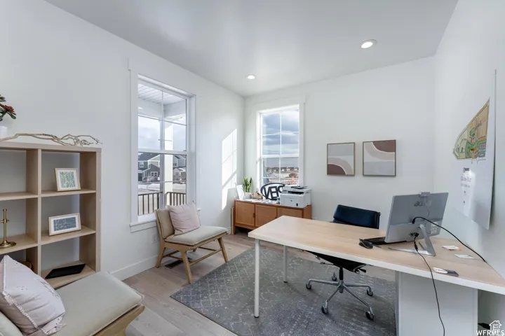 Recessed lighting illuminates this bright space, featuring two large windows, light wood-finish flooring, and white painted walls