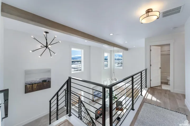 Upper landing with wood-finish flooring, recessed lighting, and a modern linear chandelier
