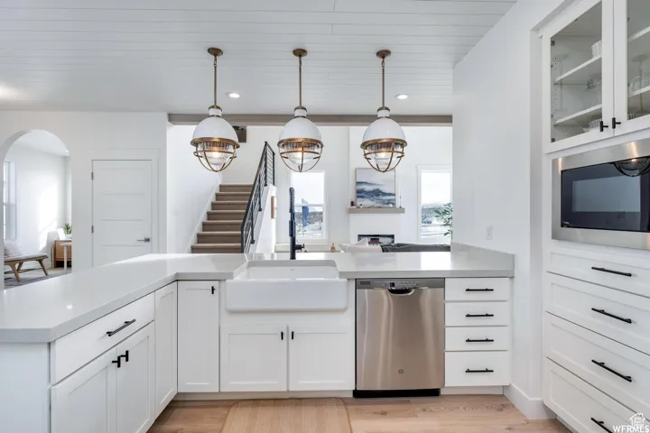 White shaker cabinetry, farmhouse sink, stainless steel appliances, quartz countertops, and wood-finish flooring