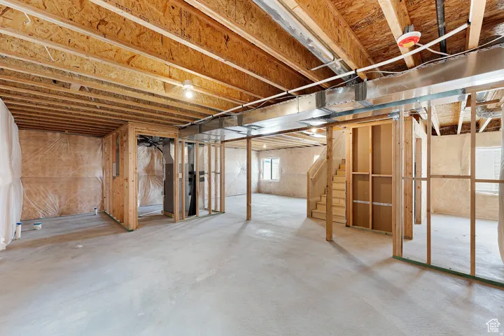 Unfinished basement featuring exposed wood joists, concrete flooring, framed interior walls, and utility access