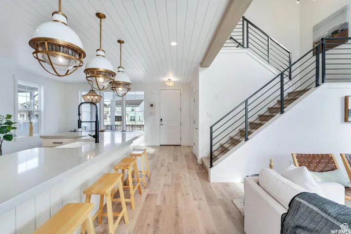 Expansive living area with wood-finish flooring, a contemporary staircase with metal railings, and a kitchen island with stone countertops
