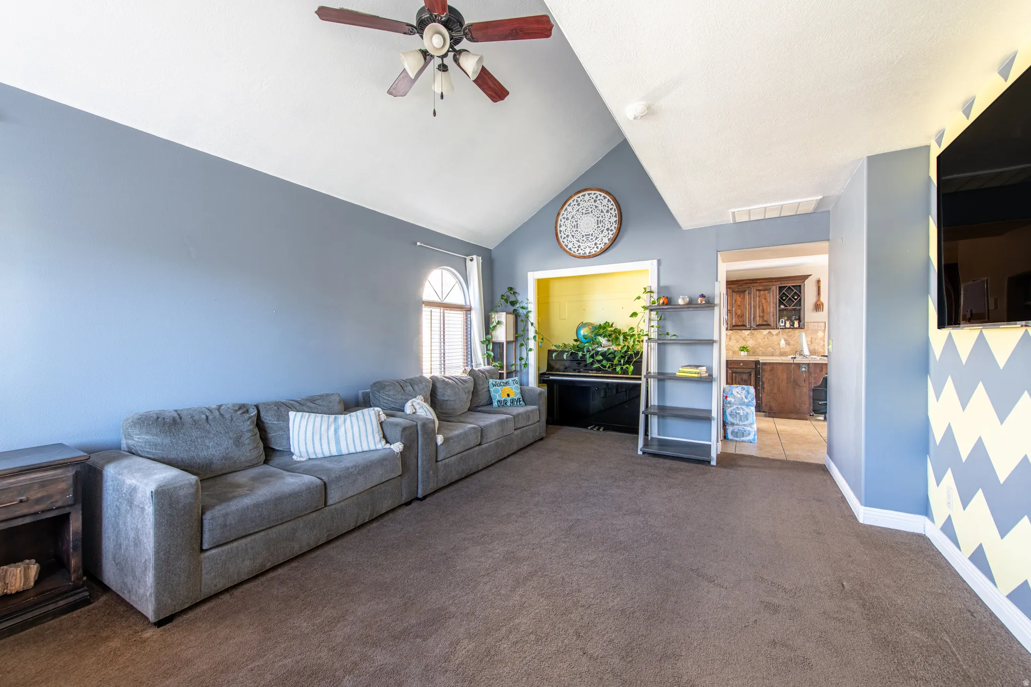 Vaulted ceiling with a ceiling fan, arched window, and carpeted flooring