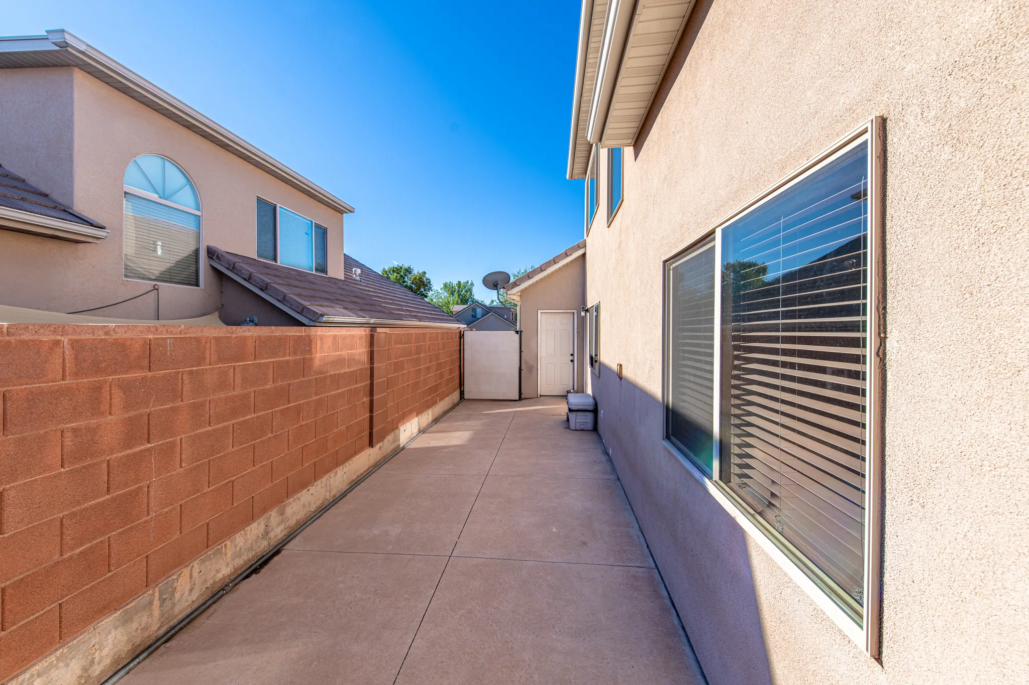 Paved concrete pathway with a high block wall, stucco exterior, and multiple windows