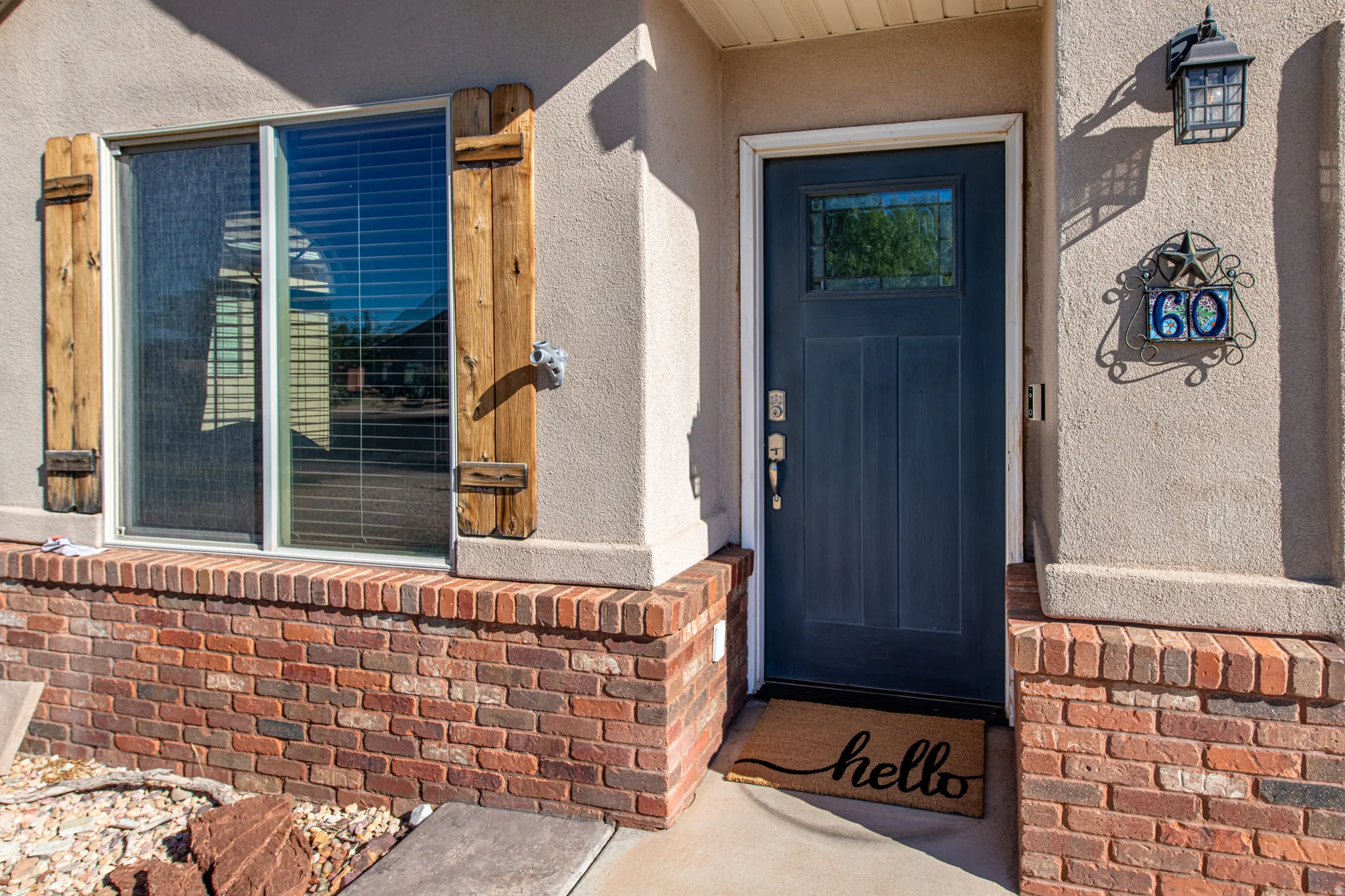 Stucco exterior with brick detailing, dark blue entry door with glass insert, and exterior wall sconce