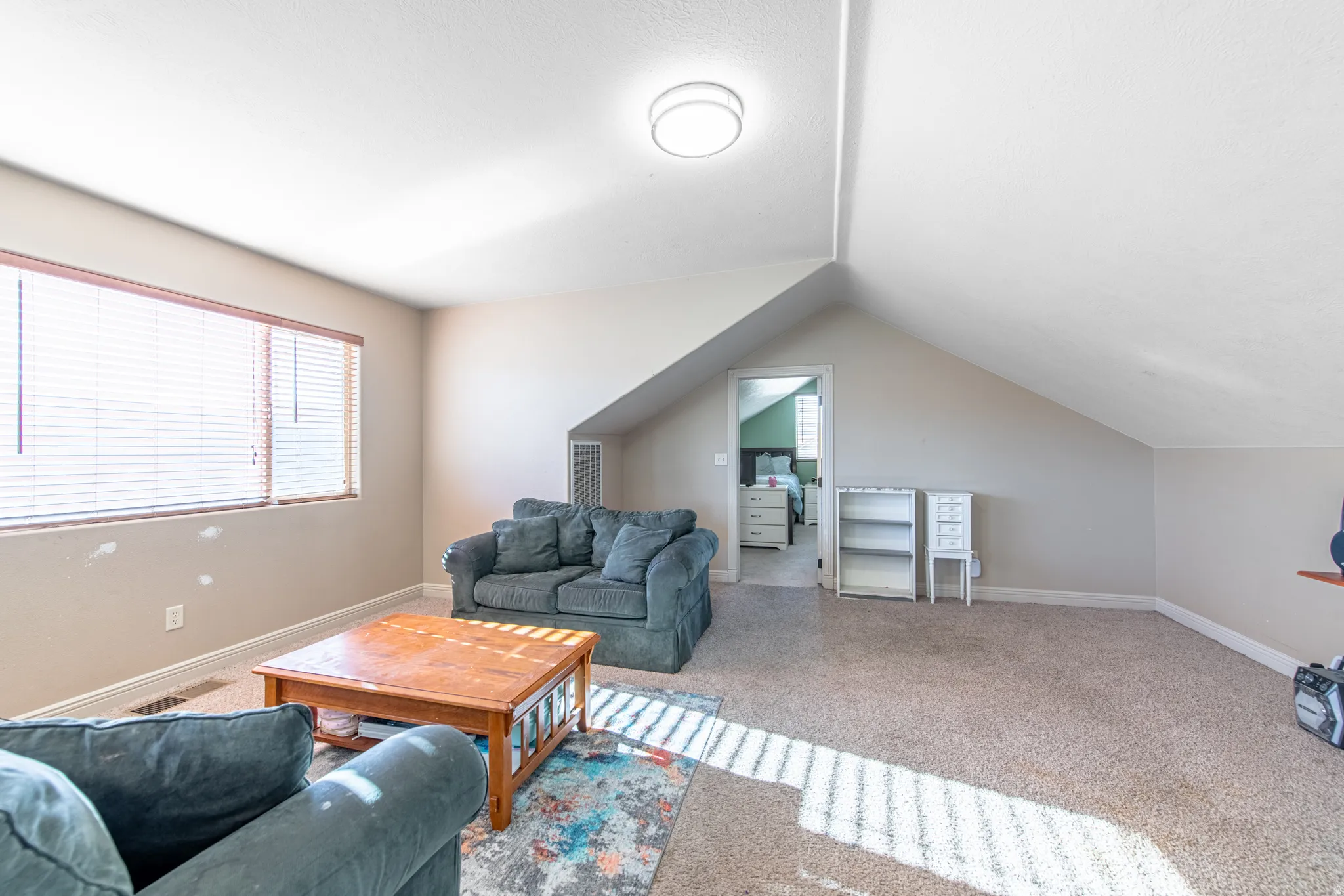 Carpeted room with sloped ceilings, natural light from a large window, recessed lighting, and a neutral color palette