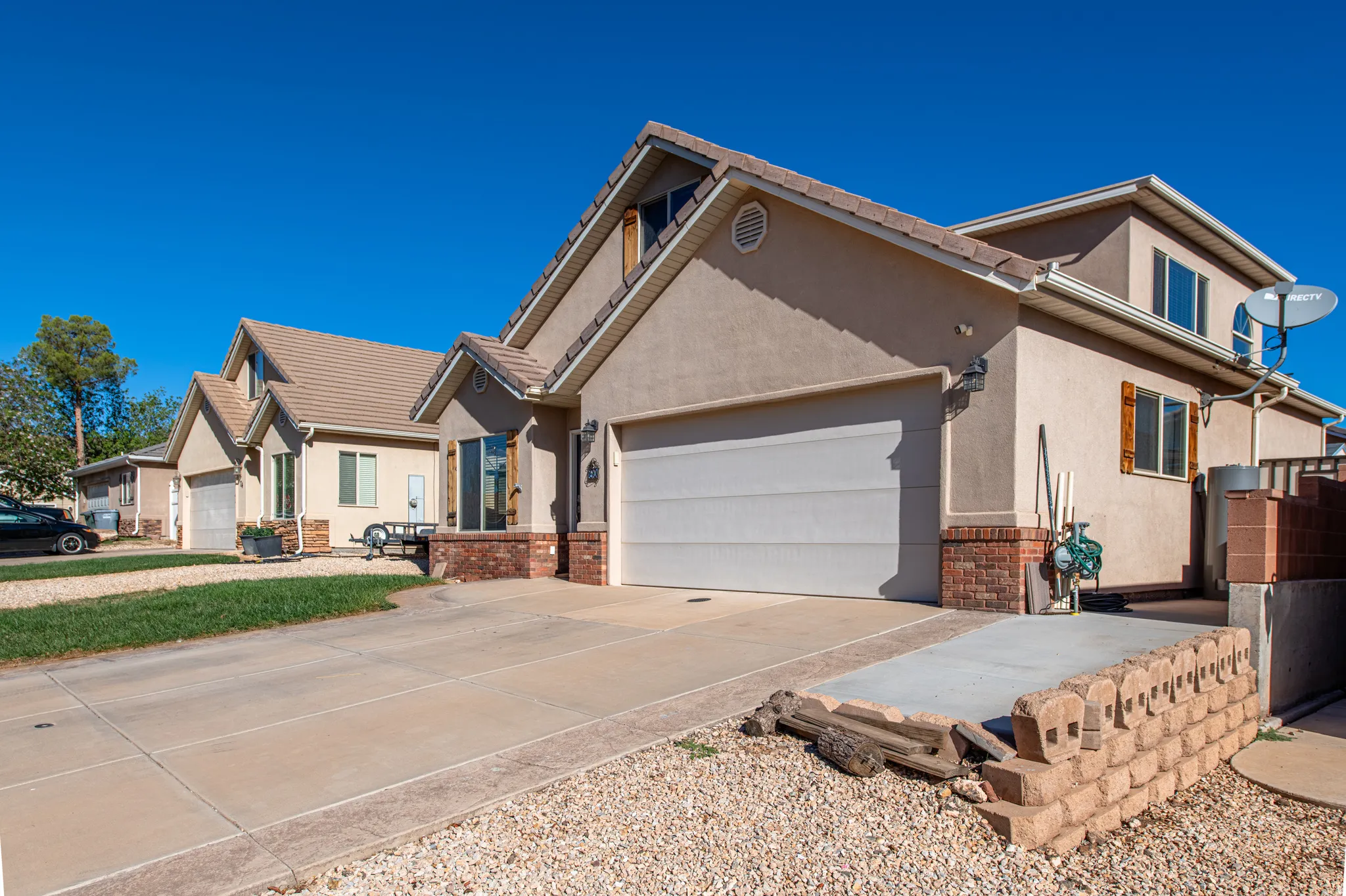 Stucco exterior with brick detailing, attached garage, concrete driveway, and a retaining wall