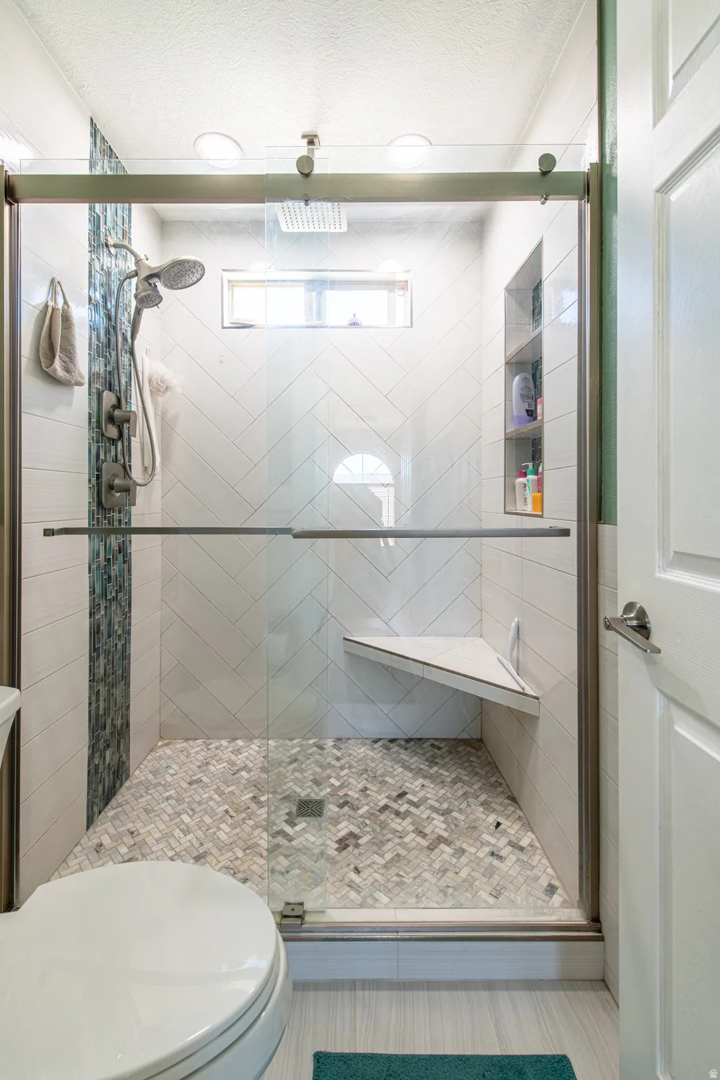 Frameless glass shower enclosure with a herringbone tile floor, built-in corner bench, and integrated niche shelving