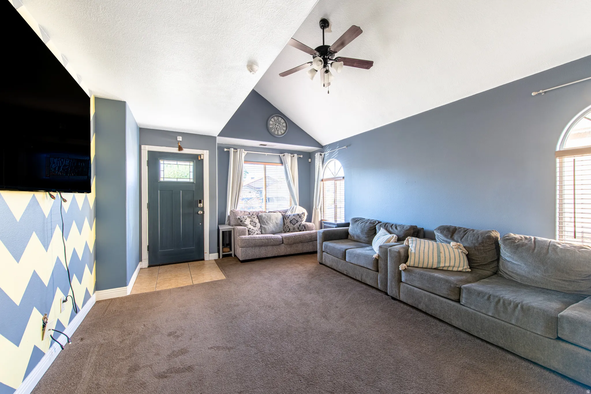 Vaulted ceilings with a ceiling fan, arched windows, and a panel entry door with an upper glass insert