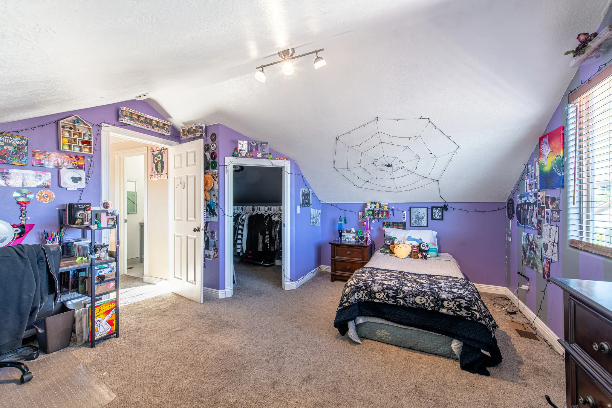 Carpeted flooring, sloped ceiling, track lighting, and a window with blinds