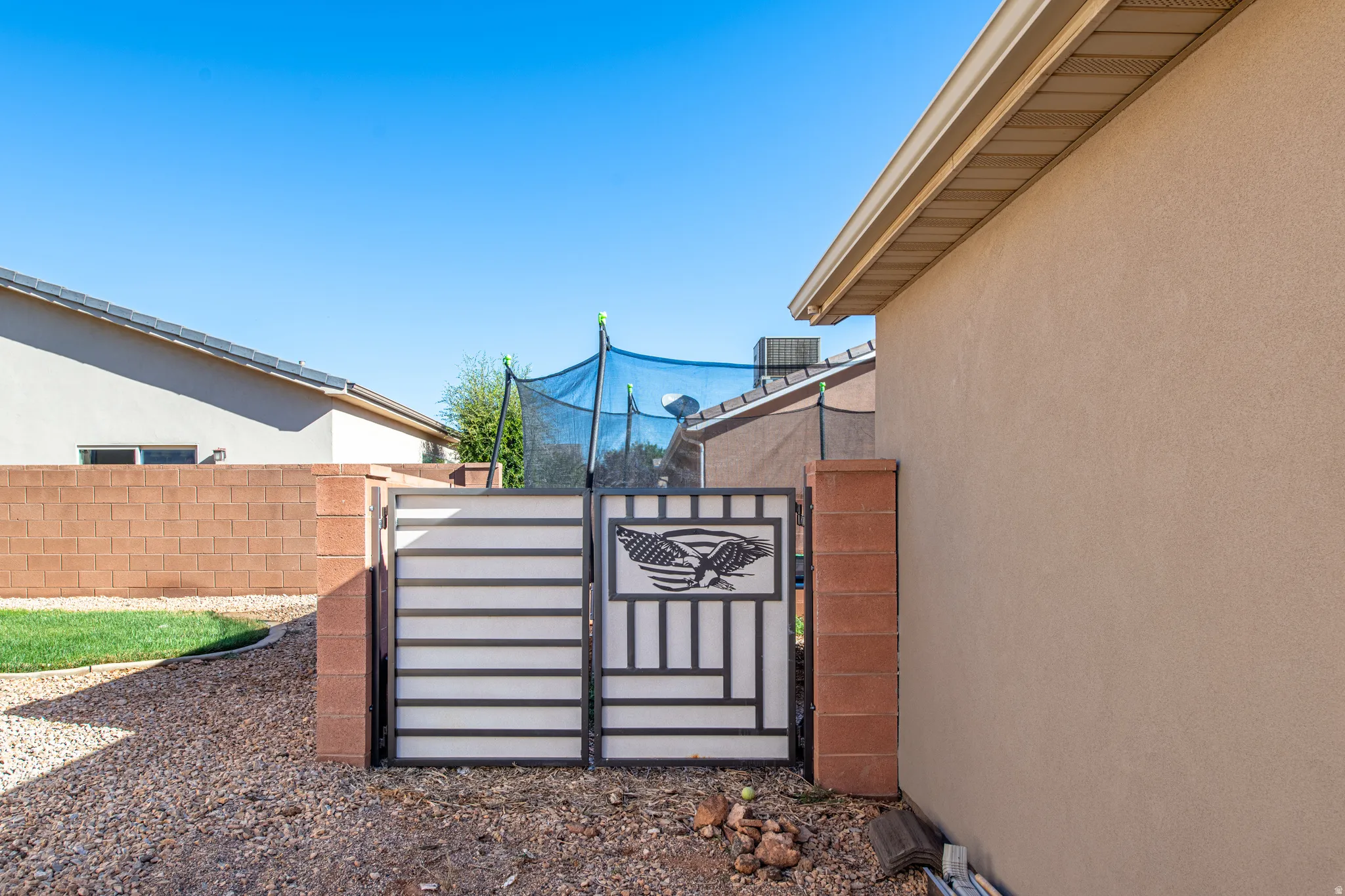 Stucco exterior with a tan finish, accented by a decorative metal gate featuring an eagle motif, and a brick-block privacy wall