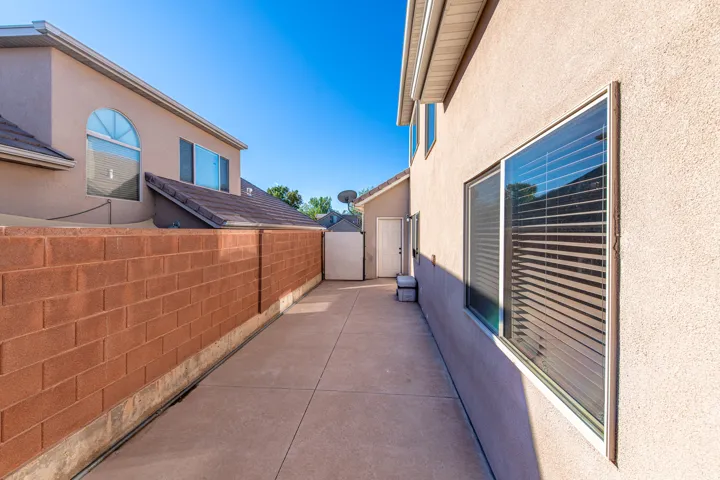 Paved concrete pathway with a high block wall, stucco exterior, and multiple windows