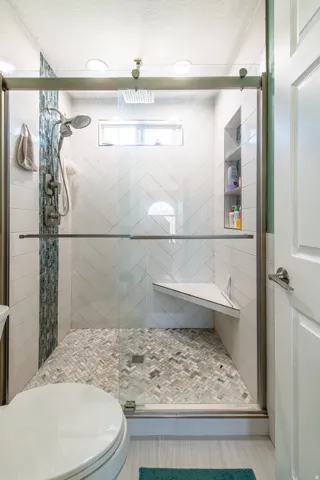 Frameless glass shower enclosure with a herringbone tile floor, built-in corner bench, and integrated niche shelving