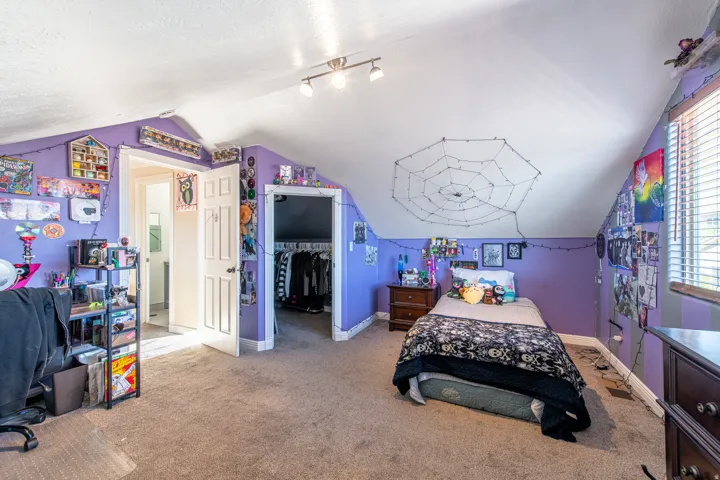 Carpeted flooring, sloped ceiling, track lighting, and a window with blinds
