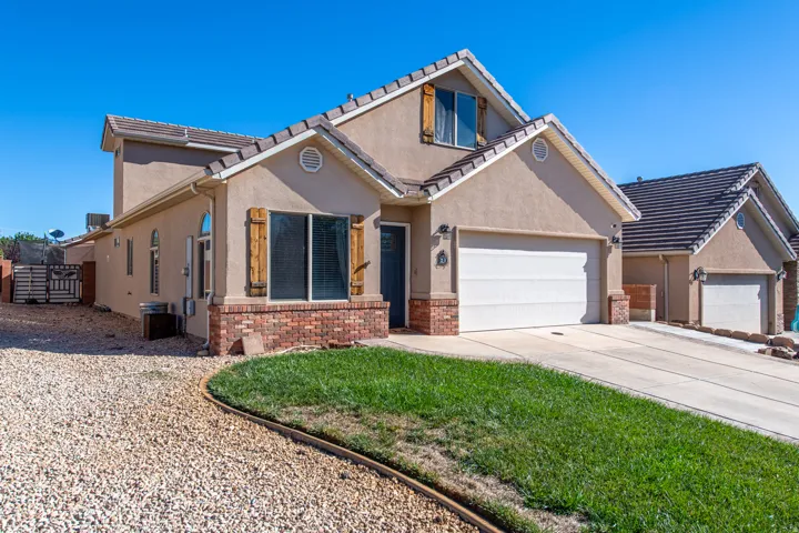 Stucco exterior with brick detailing, wood-finish window shutters, an attached two-car garage, and a concrete driveway