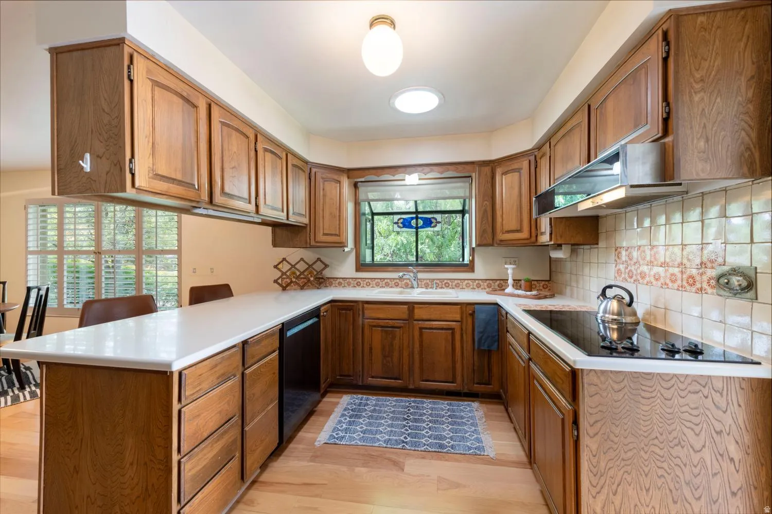 U-shaped kitchen featuring wood cabinetry, light-toned countertops, a built-in cooktop, and a tile backsplash