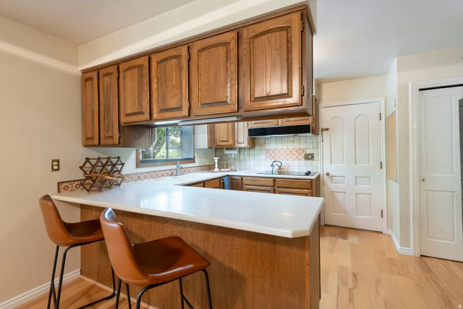 Kitchen featuring wood cabinetry, light-toned countertops, a tile backsplash, and light wood-finish flooring