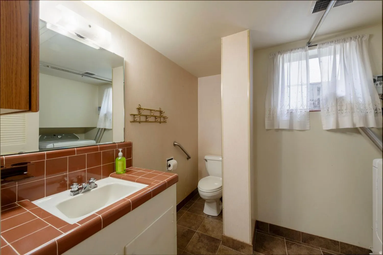 Built-in vanity with a tiled countertop, wall-mounted mirror with overhead lighting, and a window with natural light