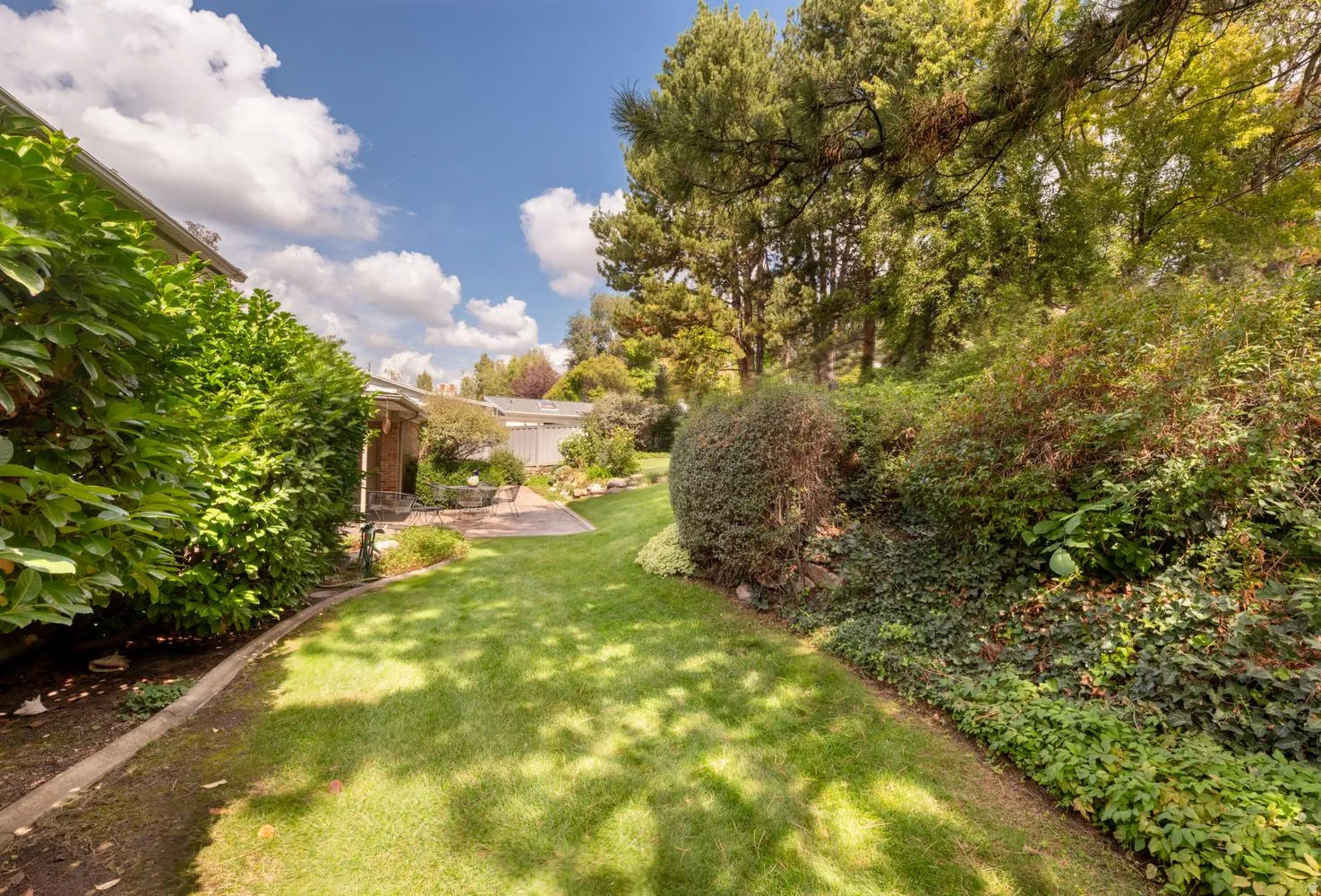 Expansive lawn area with mature trees, established shrubbery, and a stone patio