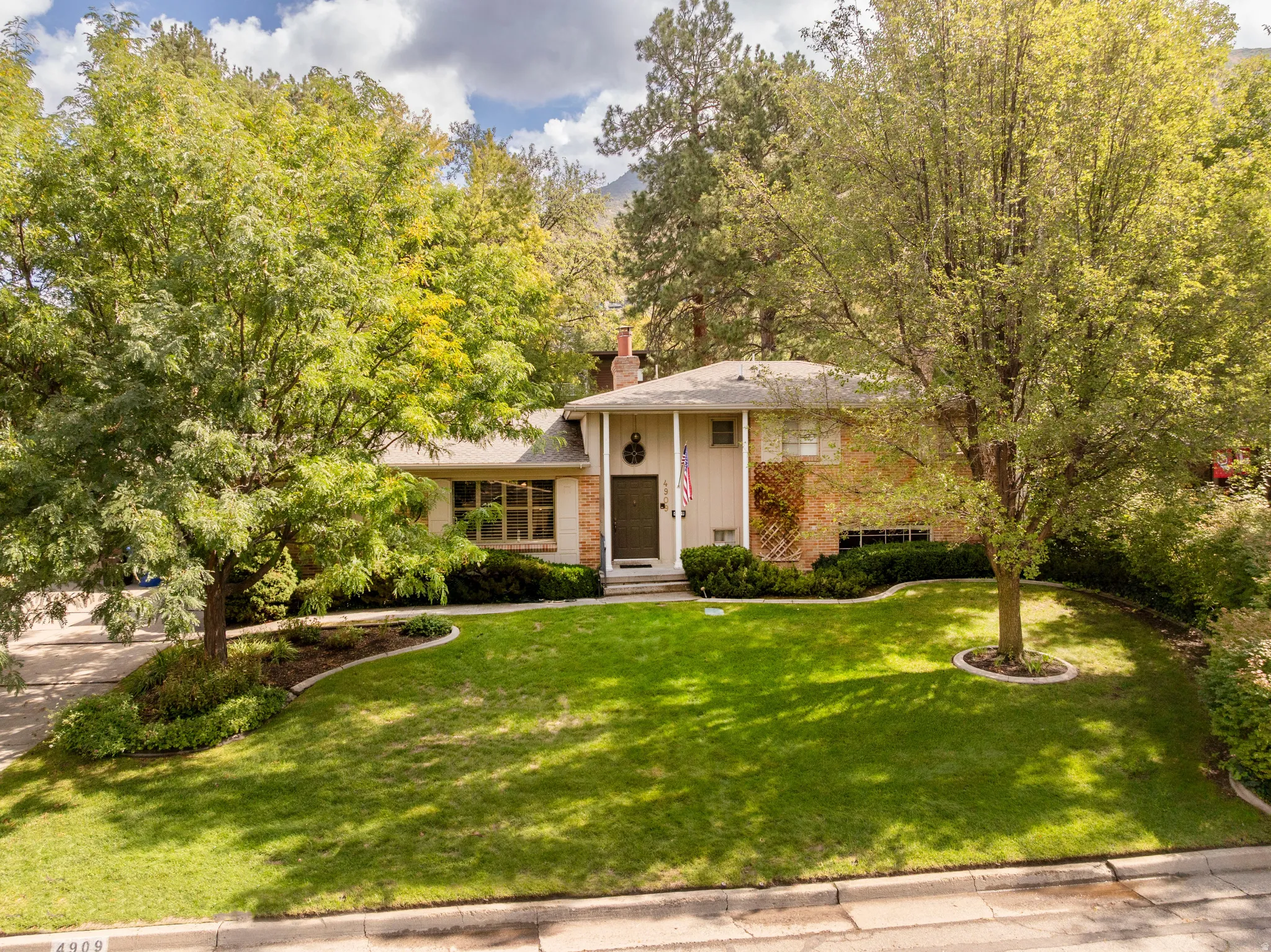 Traditional-style residence featuring a brick and siding exterior, front lawn, mature trees, and established landscaping