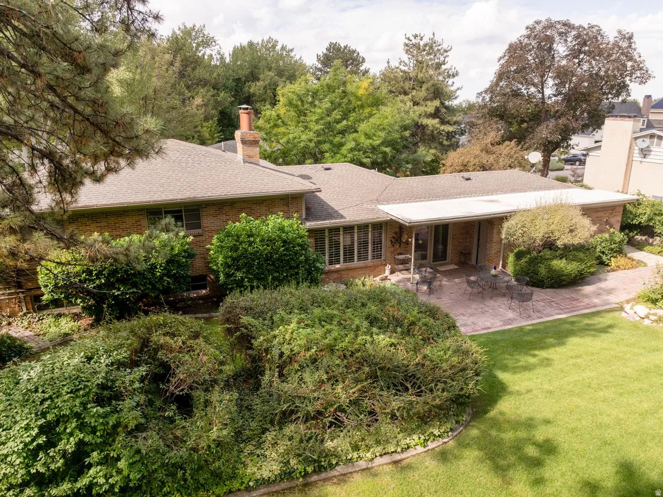 Brick exterior with a covered patio, a stone paver pathway, mature landscaping, and an expansive lawn