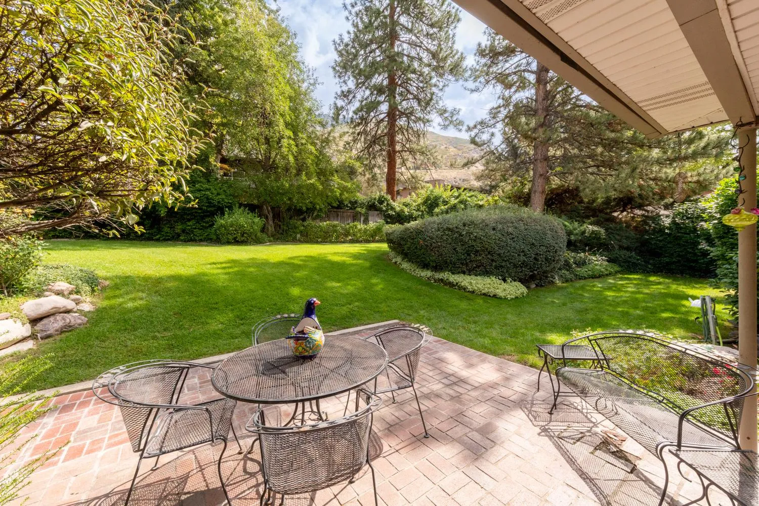 Expansive lawn area with mature trees and established landscaping, featuring a brick paver patio and a covered outdoor space