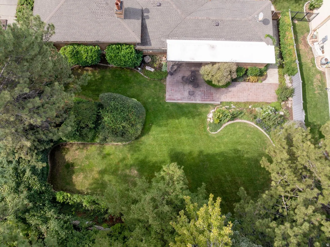 Expansive backyard featuring a large green lawn, mature trees, and a brick patio with an overhead cover