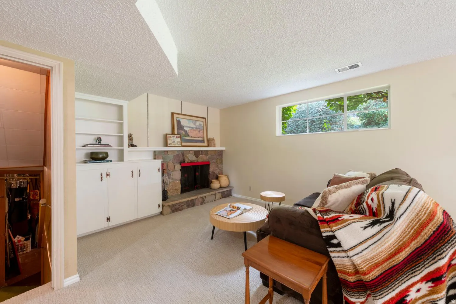 Stone-clad fireplace with a raised hearth, built-in shelving, white cabinetry, and carpeted flooring