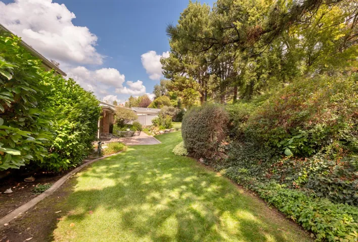 Expansive lawn area with mature trees, established shrubbery, and a stone patio