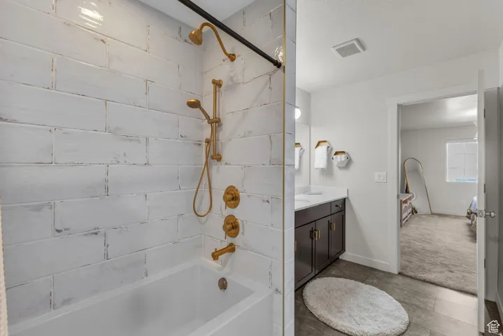Bathtub and shower combination with white subway tile surround, gold-tone fixtures, and a dark wood-finish vanity with dual sinks