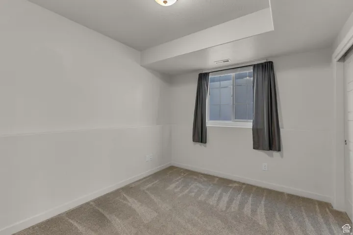 Interior room with neutral carpet flooring, a window with window treatments, and white paneled walls