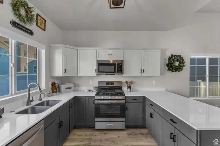 U-shaped kitchen featuring two-tone cabinetry, light-toned countertops, and wood-finish flooring