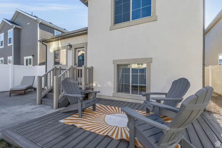 Exterior stucco finish, composite decking, outdoor stairs with railing, white vinyl fencing, and a ground-level concrete patio