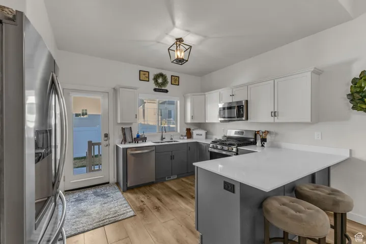 Kitchen featuring wood-finish flooring, two-tone cabinetry with upper white and lower gray finishes, stainless steel appliances, and light-toned countertops