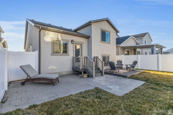 Private outdoor space featuring a composite deck, a concrete patio, a white vinyl fence, and a stucco exterior
