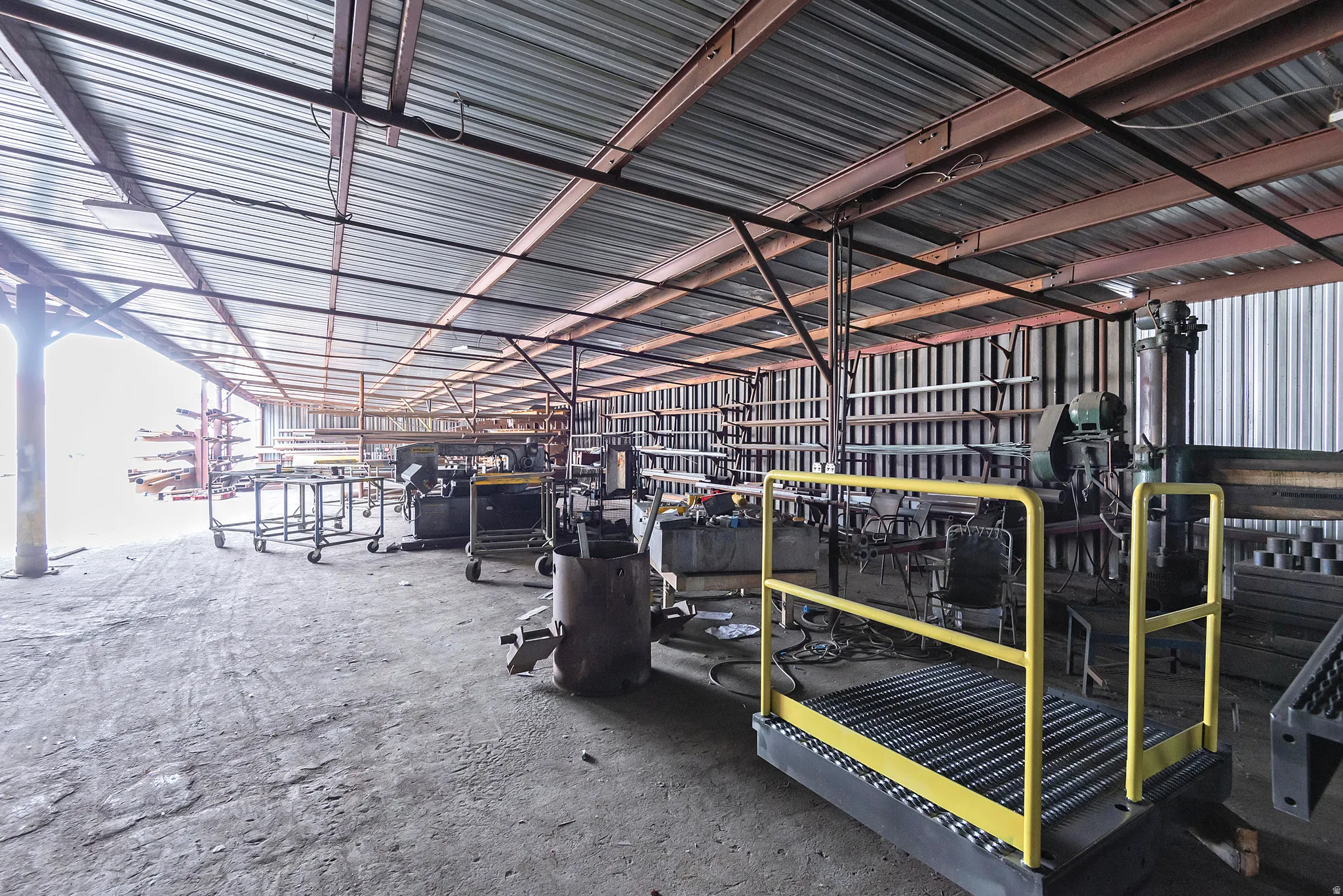 Corrugated metal roof, exposed structural beams, concrete flooring, and extensive open space
