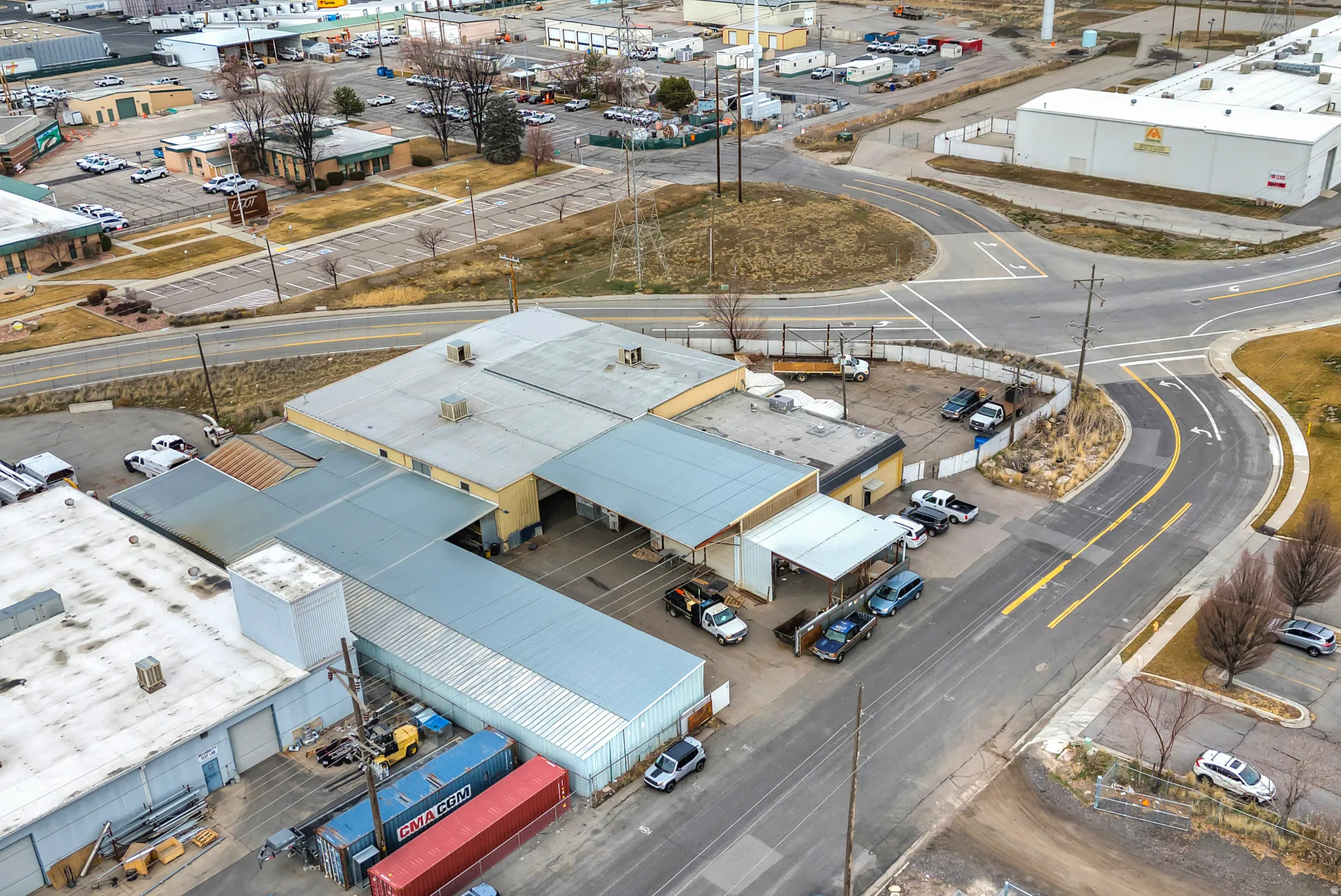 Industrial building featuring multiple rooflines, an attached covered parking area, and a paved lot