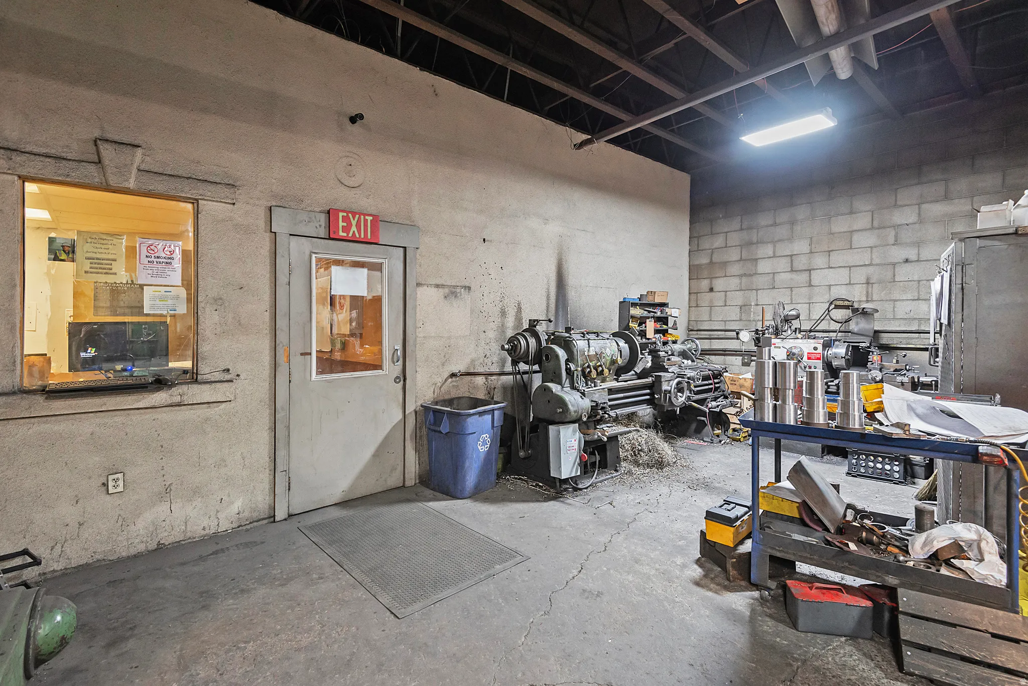 Concrete block walls, exposed ceiling joists, concrete flooring, illuminated light fixture, and a service window