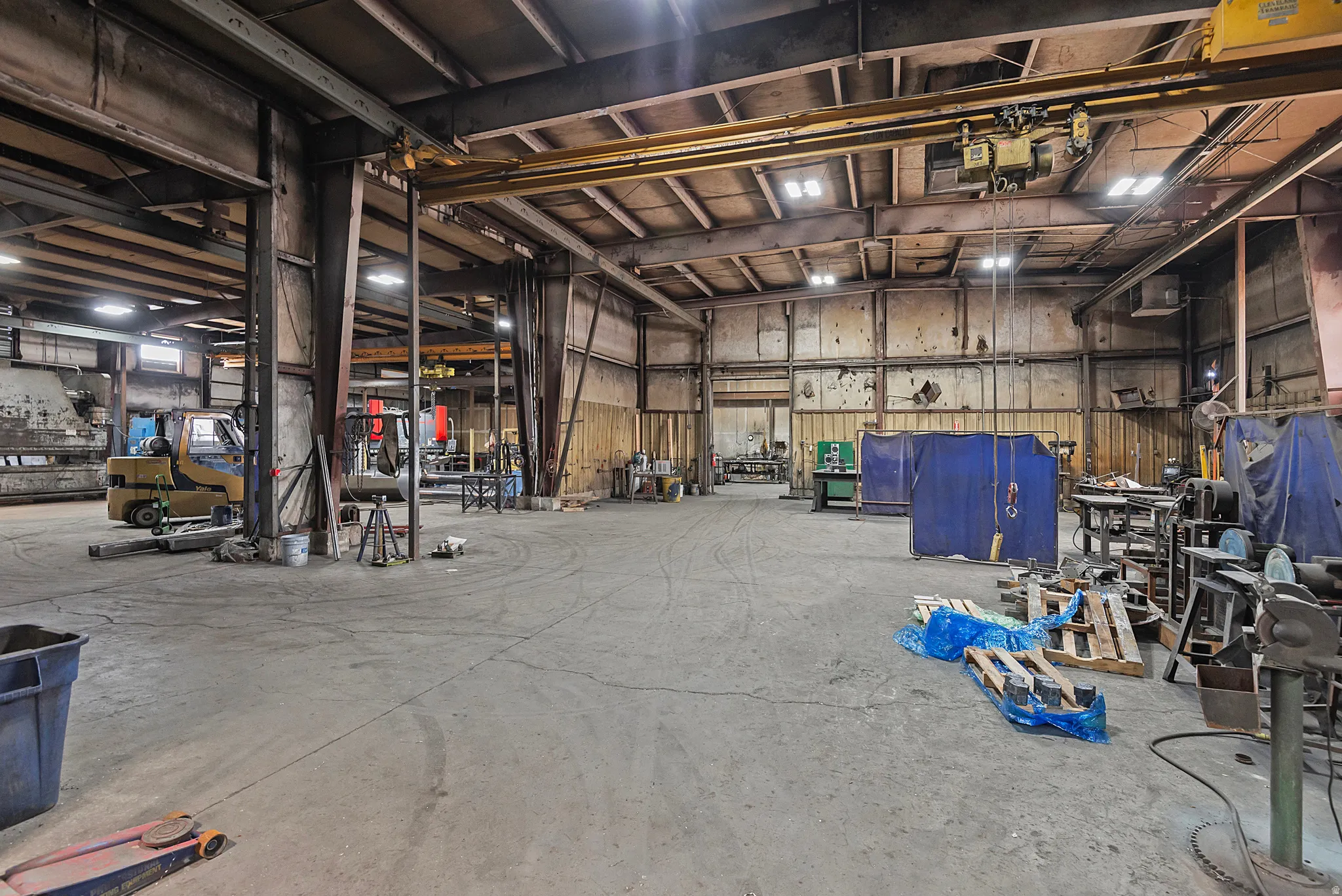 Spacious industrial interior featuring a concrete floor, exposed metal structural beams, overhead cranes, and high ceilings